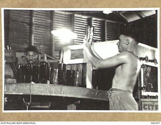 17 MILE, LALOKI RIVER, NEW GUINEA. 1943-11-22. S60128 PRIVATE G. SCHMIDT CHECKING BOTTLES FOR CLEANLINESS, AS THEY ARE REMOVED FROM THE BOTTLE WASHING MACHINE AT THE CORDIAL FACTORY ESTABLISHED AND ..