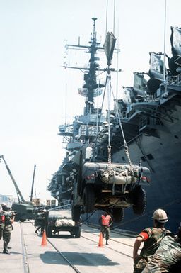 An M-998 multi-purpose wheeled vehicle is loaded aboard the amphibious assault ship USS GUAM (LPH 9) as equipment of the 2nd Marine Division is readied for transport to the Middle East in support of Operation DESERT SHIELD