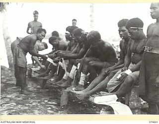 MALAMAL, NEW GUINEA. 1944-07-13. QX218 CORPORAL P. MURPHY, QUARTERMASTER AND A NATIVE "LIK-LIK DOCTOR" (SMALL DOCTOR OR MEDICAL ORDERLY) TREATING NATIVES ATTENDING THE SICK PARADE AT THE AUSTRALIAN ..