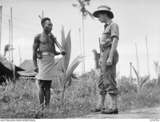 ALEXISHAFEN, NEW GUINEA. 1944-07-16. SERGEANT TAPIOLI DCM, PAPUAN INFANTRY BATTALION (1), AND SERGEANT WELLINGTON, ARMY PUBLIC RELATIONS SECTION (2), YARNING AT THE BATTALION CAMP