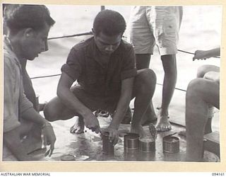 TINIAN, BOUGAINVILLE. 1945-07-18. PRIVATE J. SARELA, NETHERLANDS EAST INDIES ARMY, OPENING CANS OF FOOD ON THE MOTOR LAUNCH ML1327. THE VESSEL IS BEING USED BY THE ALLIED INTELLIGENCE BUREAU TO ..