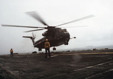 A plane director stands by as a Helicopter Mine Countermeasures Squadron 14 (HM-14) RH-53D Sea Stallion helicopter lands on the flight deck of the amphibious assault ship USS GUAM (LPH 9)