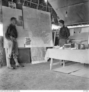 RAMU VALLEY, NEW GUINEA, 1944-03-27. VX14737 CAPTAIN G.A. WILLIAMS (1) WITH NX17 MAJOR B.H. TRAVERS, OBE, BRIGADE MAJOR (2), ALONGSIDE WALL MAPS IN THE FIELD OFFICE AT HEADQUARTERS, 15TH INFANTRY ..