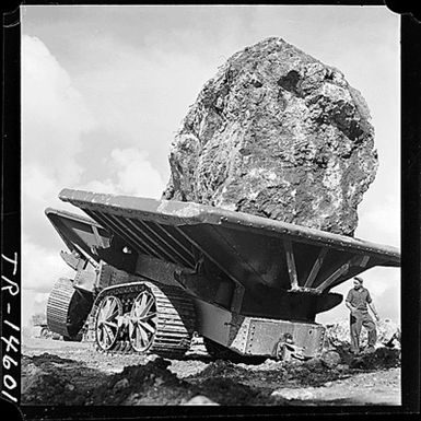 Giant seawall under construction by Seabees of the 76th Construction Battalion at Apra Harbor, Guam. When completed the two mile breakwater will contain 1, 760, 000 cubic yards of earth and stone. A 30-ton boulder is hauled to dumping spot.