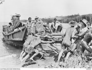 Gunners of the 2/5th Field Regiment unloading their 25 pounder gun at Biamu village. This gun is being unloaded from a Japanese barge which was captured during the abortive landing attempt at Milne ..