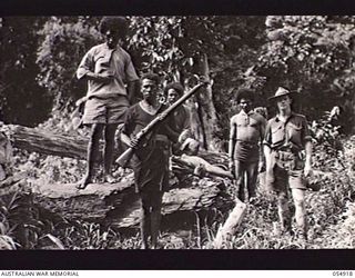 BULLDOG-WAU ROAD, NEW GUINEA, 1943-07-14. RATION CARRIERS RESTING AT THE 22 MILE POINT ON THE SURVEYED ROAD. NOTE PAPUAN POLICE BOY IN THE FOREGROUND