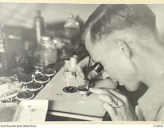 ALEXISHAFEN, NEW GUINEA. 1944-09-13. NX121429 STAFF SERGEANT J.L. MERRILL, INSTRUMENT MAKER, REPAIRING A WATCH IN THE INSTRUMENT REPAIR SHOP OF THE 133RD BRIGADE WORKSHOPS