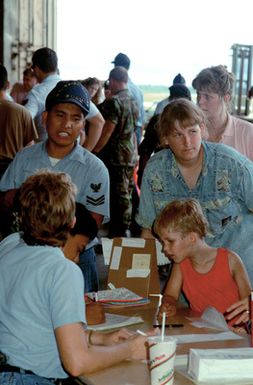 Sailors from U.S. Naval Station, Guam, work at the sign-in desk at a temporary evacuation center during Operation Fiery Vigil. The center was set up to process military dependents who were evacuated from the Philippines after volcanic ash from the eruption of Mount Pinatubo disrupted operations at Clark Air Base and Naval Station, Subic Bay.