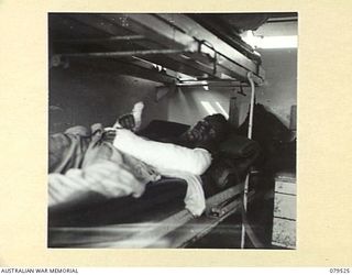 ORO BAY, NEW GUINEA. 1943-07. A WOUNDED AUSTRALIAN SOLDIER IN AN AMBULANCE OF THE 10TH FIELD AMBULANCE BEING TRANSFERRED FROM THE USS "KARU MARU" TO THE UNIT MAIN DRESSING STATION