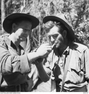 NEW GUINEA, 1943-07-27. VX90605 PRIVATE H. CARTWRIGHT (LEFT) AND VX3334 STAFF SERGEANT W. DEVERILL, OF THE 2/5TH BATTALION, ENJOY A CIGARETTE ON THE TRACK AT MOUNT TAMBU