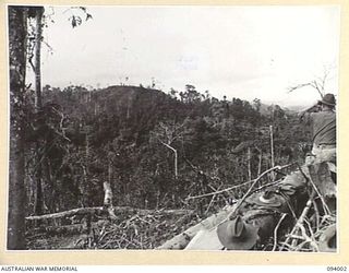 WEWAK AREA, NEW GUINEA, 1945-07-14. CAPT J.S. ADAMS, ADJUTANT, A COMPANY, 2/8 INFANTRY BATTALION (1), USING BINOCULARS AT THE COMMAND POST, WATCHES A COMPANY GAIN THE RIDGE DURING THE ADVANCE TO ..