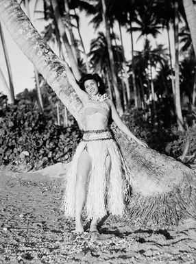 [Pacific Island woman poses in grass skirt against tree]