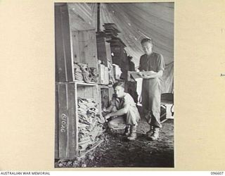 CAPE WOM, WEWAK AREA, NEW GUINEA. 1945-09-15. PRIVATE D. SWAN (1) AND STAFF SERGEANT C. SPIERS (2), MEMBERS OF HEADQUARTERS 6 DIVISION, MAKING A STOCK CHECK ON CLOTHING IN THE QUARTERMASTER'S STORE