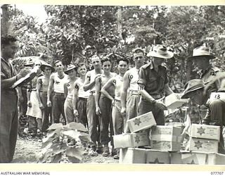 BOUGAINVILLE ISLAND. 1944-12-24. PERSONNEL OF THE 9TH INFANTRY BATTALION RECEIVING THEIR ISSUE OF AUSTRALIAN COMFORTS FUND CHRISTMAS HAMPERS AT BATTALION HEADQUARTERS. IDENTIFIED PERSONNEL ARE:- ..