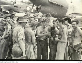 KIRIWINA, TROBRIAND ISLANDS, PAPUA. 1943-11-12. AIRMEN OF NO. 76 (KITTYHAWK) SQUADRON RAAF AT "SMOKO" TIME STANDING IN A GROUP IN FRONT OF THE AIRCRAFT TO GET A LIGHT FROM AN AIRMEN WITH A PETROL ..