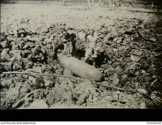 Port Moresby, New Guinea. 1943. Members of a RAAF Bomb Disposal Unit, Lazarini (left) and Neville John Young stand with a 2000lb United States bomb amidst the rubble and ruin left after a fire in ..