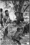 Pig festival, pig sacrifice, Tsembaga: man (r) holds hot stone with split wood tongs, others mix food on banana leaves