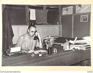 LAE AREA, NEW GUINEA. 1945-08-31. MAJOR G.F. JENKINSON, COMMANDING OFFICER 9 LINES OF COMMUNICATION STATIONERY DEPOT, WORKING IN HIS OFFICE