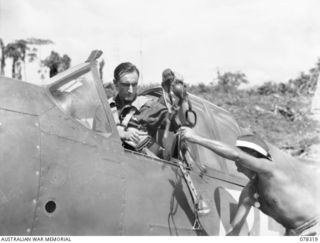 TOROKINA, BOUGAINVILLE ISLAND. 1945-01-15. 400750 FLIGHT LIEUTENANT I.C. CURTIS, NO. 5 SQUADRON, ROYAL AUSTRALIAN AIR FORCE BEING HANDED HIS FLYING HELMET BEFORE TAKING OFF IN HIS COMMONWEALTH ..