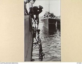 MADANG, NEW GUINEA. 1944-05-21. AUSTRALIAN TROOPS GRAPPLING FOR ABANDONED JAPANESE EQUIPMENT ALONGSIDE THE WHARF