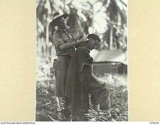 SIAR, NEW GUINEA. 1944-06-19. Q132216 PRIVATE D.S. HUSBAND (1) CUTTING THE HAIR OF VX147151 PRIVATE F.S. PETERS (2) IN THE CAMP AREA OF THE 58/59TH INFANTRY BATTALION