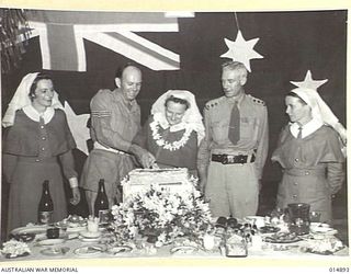 1943-05-24. NEW GUINEA. SECOND ARMY WEDDING TO BE CELEBRATED IN NEW GUINEA. CUTTING THE CAKE IS THE BRIDE, FORMERLY SISTER ALMA CRUDGINGTON, OF ROCKHAMPTON, QUEENSLAND, ASSISTED BY THE BRIDGEGROOM, ..