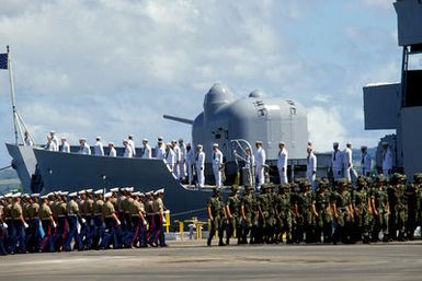 Marine Corps and Army honor guards march in formation during the designation and departure ceremony for the Unknown Serviceman of the Vietnam Era. In the background, crew members man the rails of the USS BREWTON (FF 1086). The BREWTON will transport the Unknown Serviceman to Naval Air Station, Alameda, California