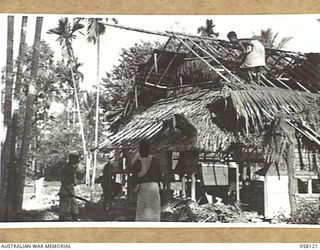 SALAMAUA, NEW GUINEA, 1943-09-26. NATIVES THATCHING THE BOMB DAMAGED ROOF OF A NATIVE HUT WITH COCONUT PALM FRONDS AFTER THE ACCEPTANCE OF THE AREA BY AUSTRALIAN AND AMERICAN TROOPS
