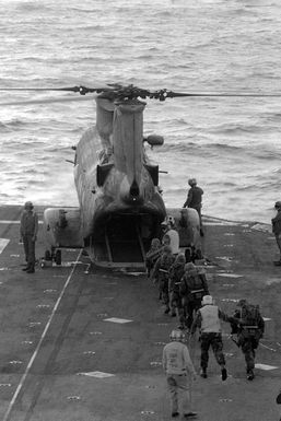 Marines go aboard a CH-46 Sea Knight helicopter on the flight deck of the amphibious assault ship USS GUAM (LPH 9) during Operation URGENT FURY