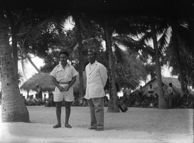 [Two Pacific island men standing underneath palm trees]