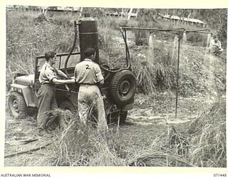 PIONEER CROSSING, PORT MORESBY AREA, PAPUA, 1944-03-25. VX68221 PRIVATE J. FORD (1), DESIGNER OF THE SHOWERS AND HEATING UNIT PICTURED WITH VX113860 CORPORAL F.J. REEVES (2), AT THE 2/107TH MOBILE ..