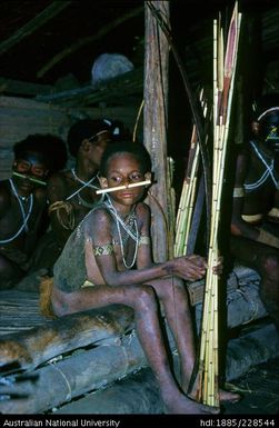 A Febi boy in his very early teens holding his bow and a sheaf of arrows while attending a late-night curing ceremony in Bulong longhouse
