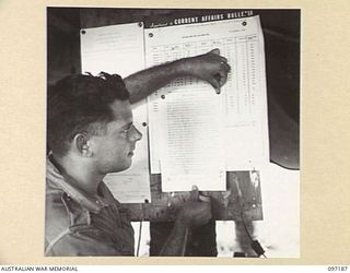 CAPE WOM, NEW GUINEA. 1945-09-27. STAFF SERGEANT K.R. OBERMAN, 110 BRIGADE ORDNANCE FIELD PARK, PINNING NOTICES ON THE UNIT NOTICE BOARD
