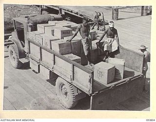 LAE AREA, NEW GUINEA, 1945-07-11. NATIVES ASSISTING WITH THE UNLOADING OF HAMPERS FROM THE LORRY TO THE WHARF DURING DISTRIBUTION OF THE MID-YEAR HAMPERS BY AUSTRALIAN COMFORTS FUND, LAE ..