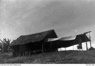 MARKHAM VALLEY AREA? NEW GUINEA. C.1945. TEMPORARY COVER ATTACHED TO A BUILDING CONSTRUCTED OF LOCAL MATERIALS WHERE MEMBERS OF THE MOBILE PROPAGANDA UNIT, FAR EASTERN LIAISON OFFICE, HELD A FILM ..