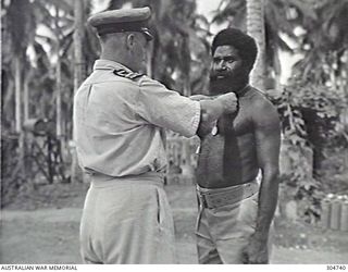 LUNGGA, GUADALCANAL, BRITISH SOLOMON ISLANDS PROTECTORATE. 1943-10-14. SERGEANT YAUWIKA RECEIVING THE LOYAL SERVICES MEDAL FROM LIEUTENANT COMMANDER I. PRYCE-JONES RANVR, THE DISTRICT SUPERVISING ..