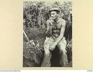 BOUGAINVILLE ISLAND, 1945-01-20. QX62647 PRIVATE R.E. BENNETS, "A" COMPANY, 42ND INFANTRY BATTALION TAKES A FEW MINUTES OFF FOR A SMOKE WHILE DIGGING FOXHOLES AT MAWARAKA