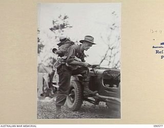 WONGINARA MISSION, NEW GUINEA. 1945-04-08. LIEUTENANT R.J. BUCHANAN, PHOTOGRAPHER, 6 MILITARY HISTORY FIELD TEAM ATTACHED HEADQUARTERS 6 DIVISION, EXAMINING PAPERS BESIDE A JEEP DURING OPERATIONS ..