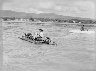 [View of man holding fish in a canoe taken from on board a ship]