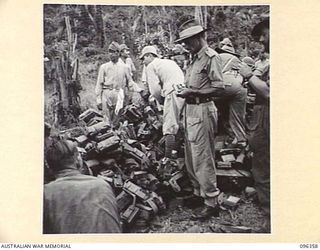 KAIRIRU ISLAND, NEW GUINEA, 1945-09-08. CAPTAIN F.E. COLLINGS, ALLIED TRANSLATER AND INTERPRETER SECTION, EXAMINING A JAPANESE PISTOL FOR LIVE ROUNDS WHILE JAPANESE SOLDIERS ARE LOADING EQUIPMENT ..