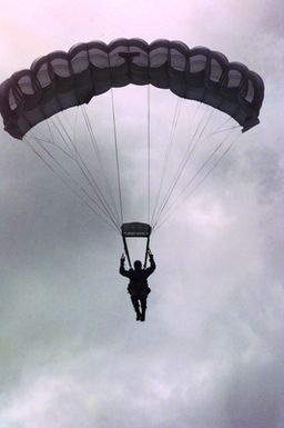 Straight on medium shot from the ground looking up at US Marine Sergeant Mark Palmer, Jumpmaster, 3rd Air Delivery Platoon, Landing Support Company, Support Battalion, 3rd Force Service Support Group, as he prepares to land safely with his MC5 Freefall Square Parachute after completing a 9-thousand foot combat jump from a USAF C-130 Hercules aircraft during the Force Reconnaissance Exercises at Andersen Air Force Base, Guam