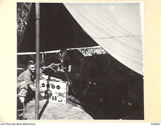 WIRUI BEACH, WEWAK, NEW GUINEA. 1945-09-04. PRIVATE J. SCIMON (1), INSPECTS A JAPANESE TRANSMITTER WHILE CORPORAL G. BENNETT (2), ADJUSTS A JAPANESE LIGHTING MOTOR