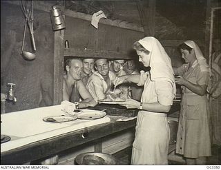 MADANG, NEW GUINEA. C. 1945. 501392 SISTER M. WITCOMBE OF SYDNEY, NSW, AND 500368 SISTER P. FEWKES OF MELBOURNE, VIC, SERVE MEALS TO HUNGRY PATIENTS FROM THE HOSPITAL KITCHEN AT NO. 1 MEDICAL ..