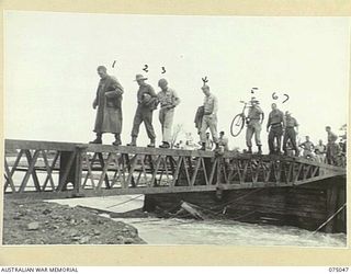 LAE, NEW GUINEA. 1944-08-09. AUSTRALIAN AND AMERICAN TROOPS CROSSING THE FIRST SPAN OF THE NEW BRIDGE ACROSS THE BUTIBUM RIVER WHICH IS BEING BUILT BY THE 20TH FIELD COMPANY, TO REPLACE THE OLD ..