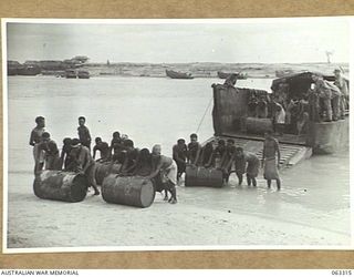 SIALUM BEACH, NEW GUINEA. 1944-01-07. NATIVES UNLOADING 44 GALLON DRUMS FULL OF PETROL AND OIL FROM THE LCM (LANDING CRAFT MECHANISED) AT THE BEACH