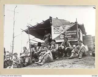 BERRY'S HILL, CENTRAL BOUGAINVILLE, 1945-06-27. THE YMCA - AUSTRALIAN COMFORTS FUND TEA POINT ON BERRY'S HILL. SHOWN ARE TROOPS OF 7 INFANTRY BATTALION HAVING A CUP OF TEA. A HUNDRED GALLONS OF TEA ..