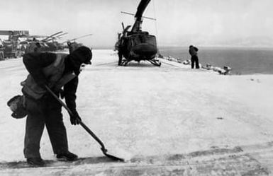 A crewman clears snow from the flight deck of the amphibious assault ship USS GUAM (LPH-9) during the NATO exercise Cold Winter (COLDEX-FLOTEX '81). The exercise is intended to test all phases of amphibious operations in sub-freezing weather