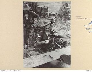 WEWAK AREA, NEW GUINEA, 1945-06-07. LANCE-CORPORAL D.W. HOWARD, 2/3 FIELD REGIMENT (1), FITS THE DIAL SIGHT TO A 25-POUNDER WHILE SERGEANT E.L. BUXTON, GUN SERGEANT (2), WATCHES PROCEEDINGS