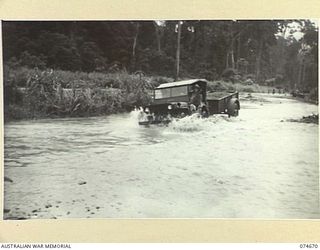 LAE-NADZAB, NEW GUINEA. 1944-07-19. AN AUSTRALIAN SOLDIER TRYING TO NEGOTIATE A BADLY FLOODED SECTION OF THE LAE-NADZAB ROAD WITH HIS JEEP AND TRAILER