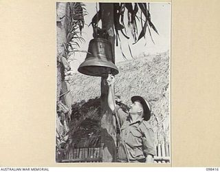 RABAUL, NEW BRITAIN. 1945-10-30. PRIVATE C. CAMERON, HEADQUARTERS 11 DIVISION, RINGING THE CHAPEL BELL SUMMONING TROOPS TO THE SERVICE. THIS BELL IS A RELIC OF AN OLD MISSION IN THE AREA